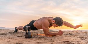 muscular hispanic man doing plank on the beach at sunrise