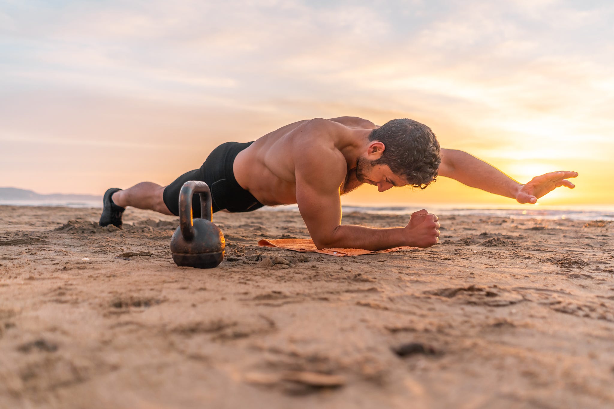 muscular hispanic man doing plank on the beach at sunrise