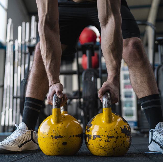 muscular male athlete holding kettlebells in gym