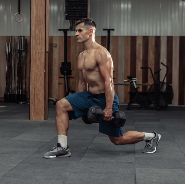 muscular man training his legs, doing lunges with heavy dumbbells in modern gym healthy lifestyle concept