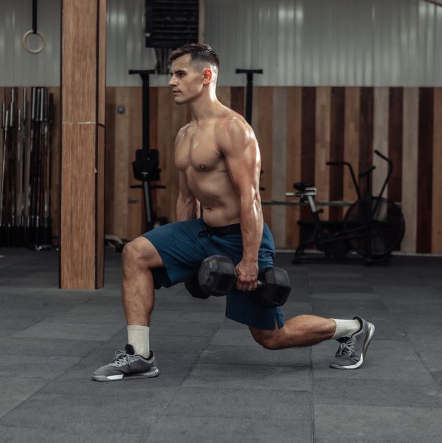 muscular man training his legs, doing lunges with heavy dumbbells in modern gym healthy lifestyle concept