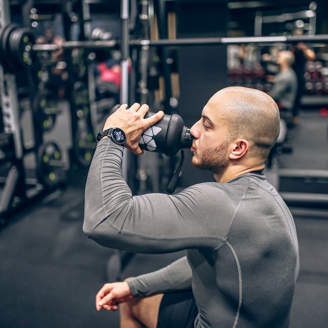 muscular men drink his nutritional supplement in gym