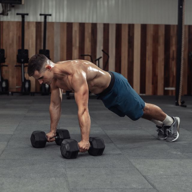 muscular powerful man doing press ups with dumbbells in gym