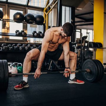 muscular shirtless man exercising with weights in gym
