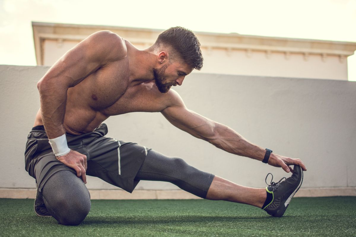 Muscular shirtless sportsman stretching legs before training outdoors