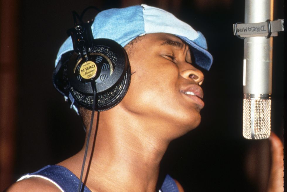 usher wearing a blue shirt and hat, singing into a microphone while wearing earphones