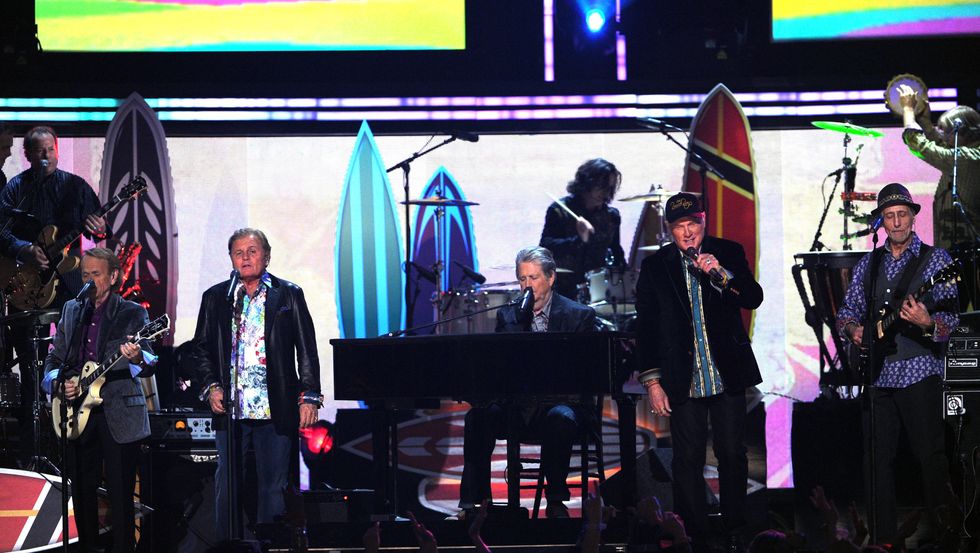 five men sing and play instruments while on a stage