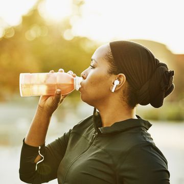 muslim woman drinking sports drink after working out in park on fall afternoon