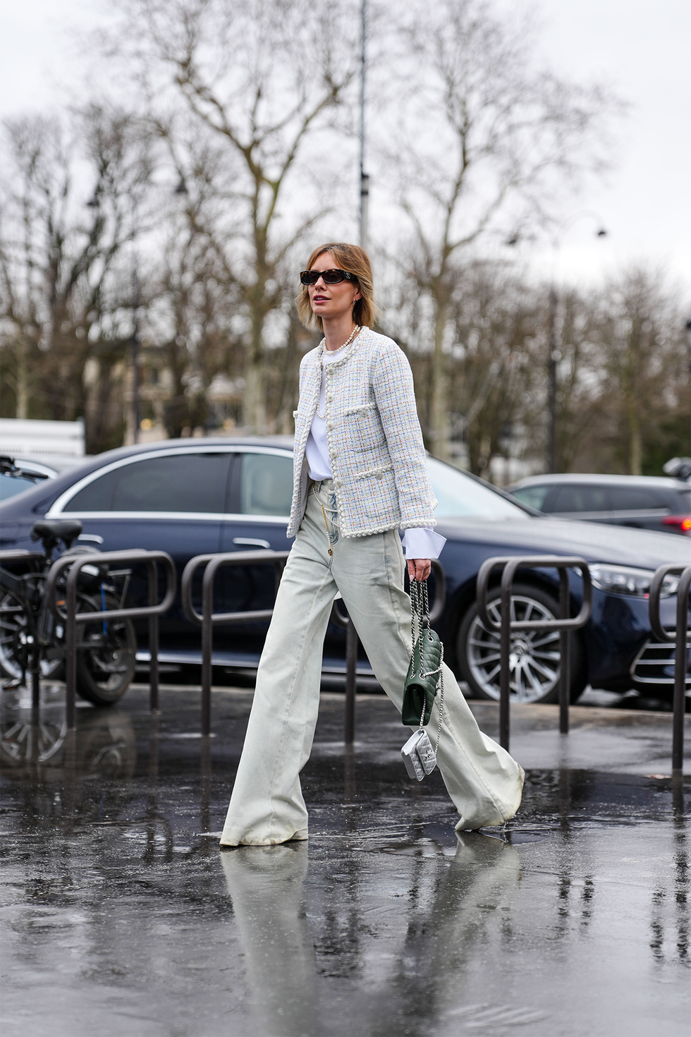 paris, france january 28: a guest wears black sunglasses, silver hoop earrings, white long sleeve shirt, white pattern chanel tweed blazer jacket, light blue baggy denim jean pants, black quilted chanel leather bag, shiny silver metallic chanel leather mini bag, outside chanel, during the haute couture spring/summer 2025 on january 28, 2025 in paris, france. (photo by edward berthelot/getty images)