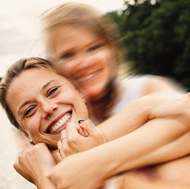 two white women laughing on a beach one has their face blurred and arms around the woman who is clearly in focus