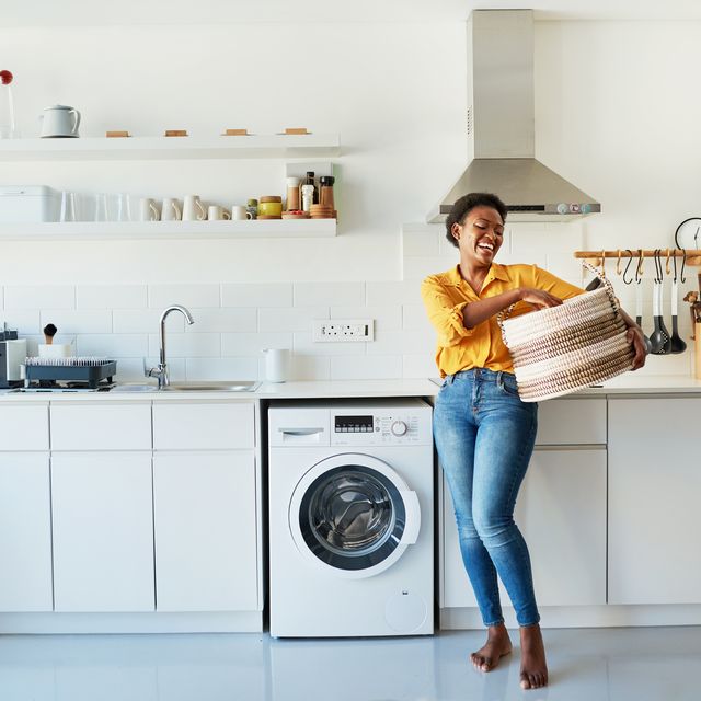 a woman holding a laundry basket next to a washing machine