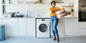 a woman holding a laundry basket next to a washing machine