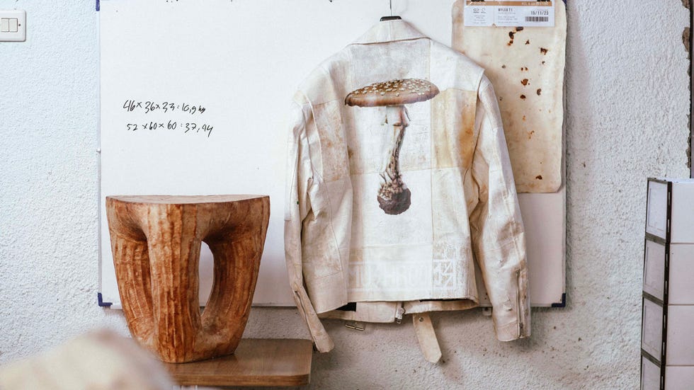 a unique jacket featuring a mushroom design hanging on a wall next to a wooden stool