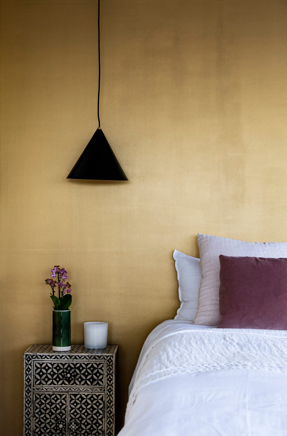 a bedroom painted in gold with nightstand and pendant lamp