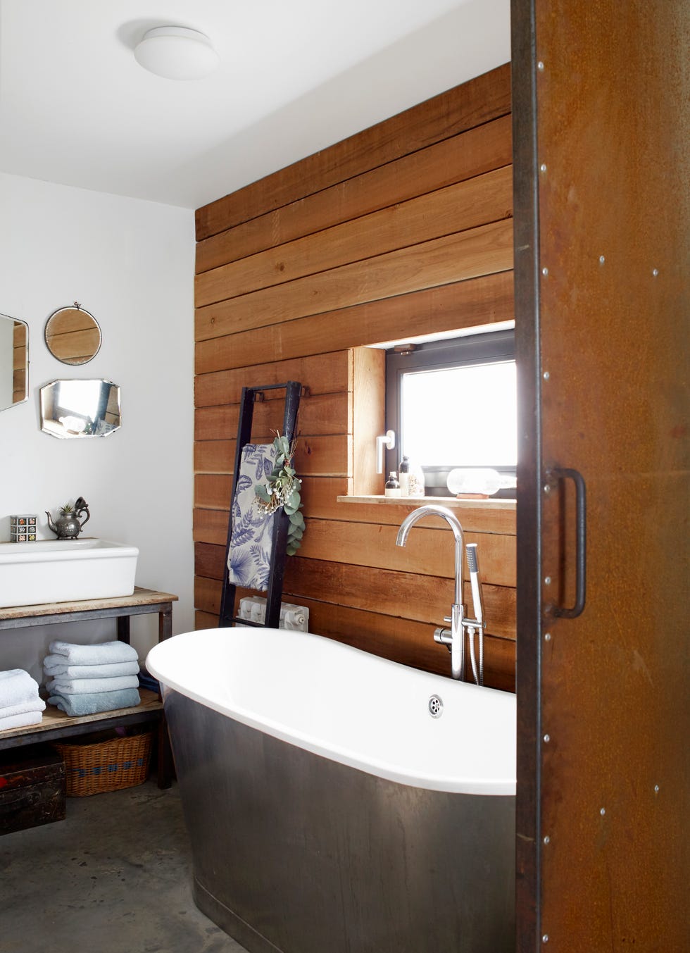 a sliding metal door left to rust naturally leads into the bathroom where one wall is covered with cedar cladding