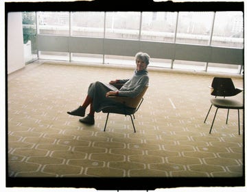 a person sitting in a chair in a spacious minimalist room with large windows