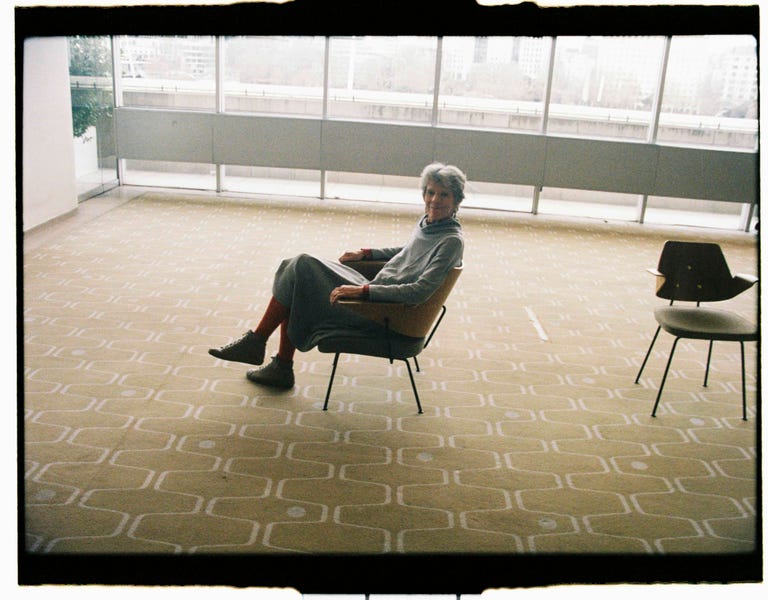 a person sitting in a chair in a spacious minimalist room with large windows