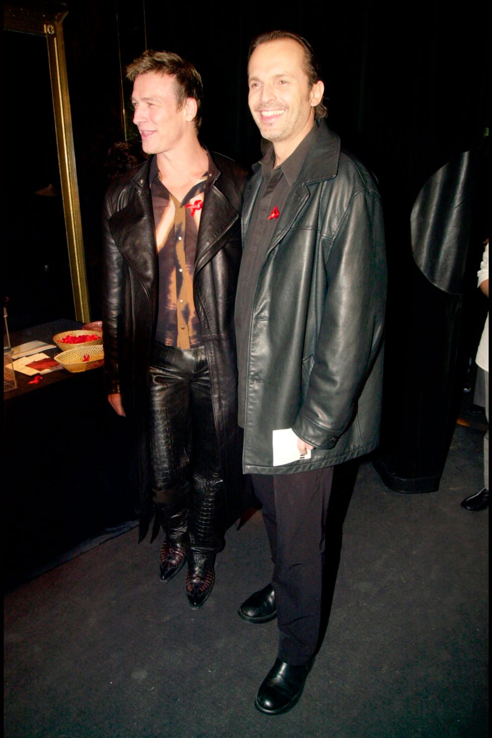 Two men standing together at an event both wearing dark leather attire