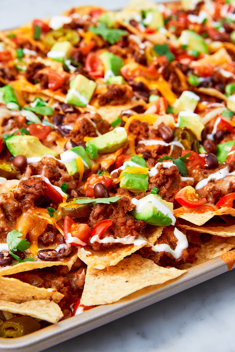 close up of nachos with black beans, tomatoes, beef, avocado, and pickled jalapenos on a sheet tray