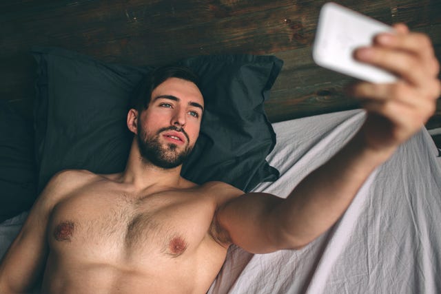 naked bearded dark hair handsome man shirtless in white bed taking a selfie