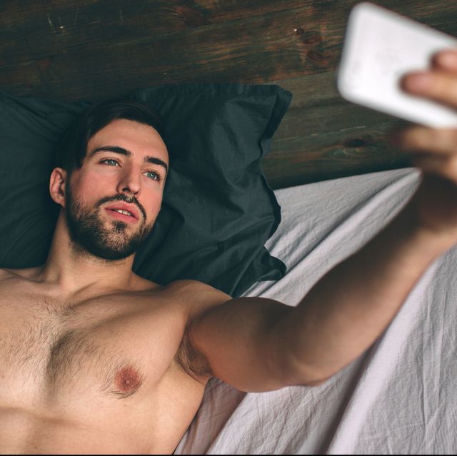 naked bearded dark hair handsome man shirtless in white bed taking a selfie