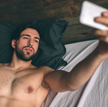 naked bearded dark hair handsome man shirtless in white bed taking a selfie