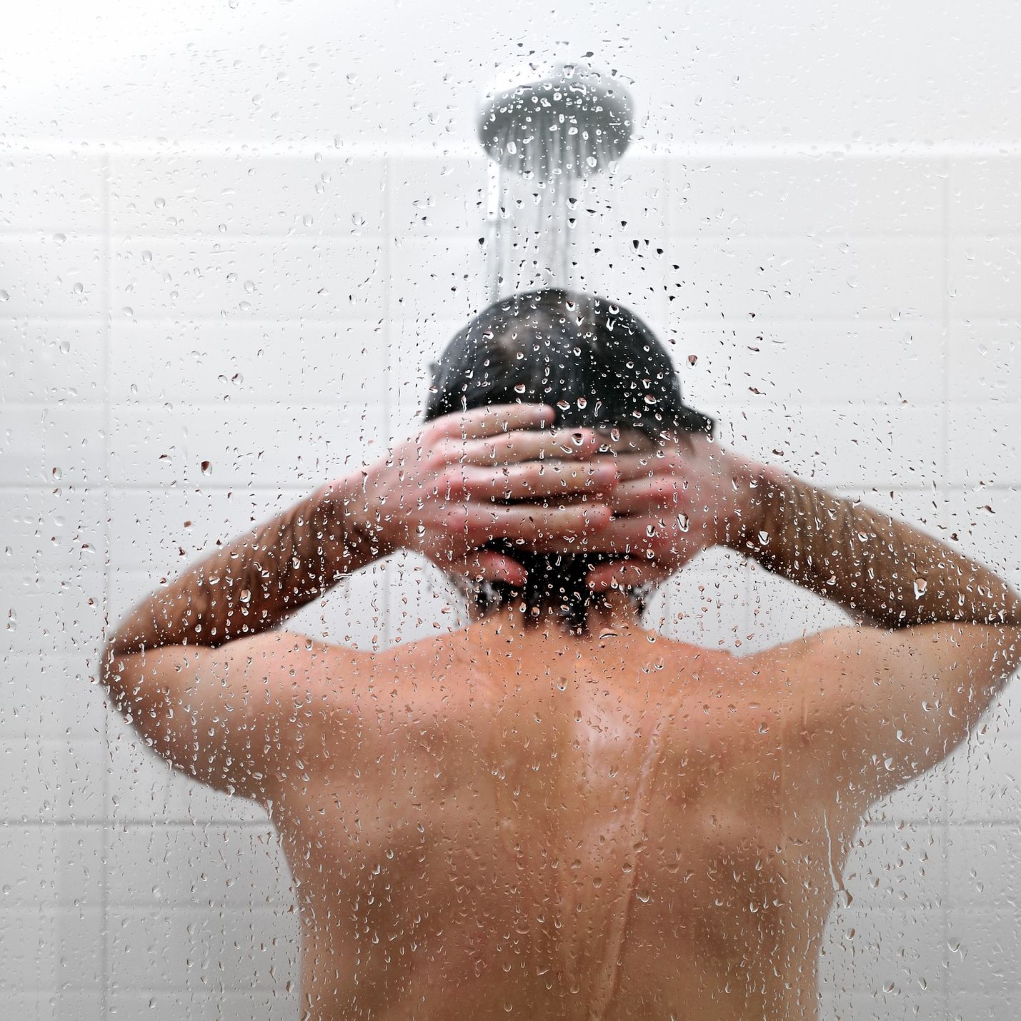 Naked man is taking a shower in bathroom, rear view