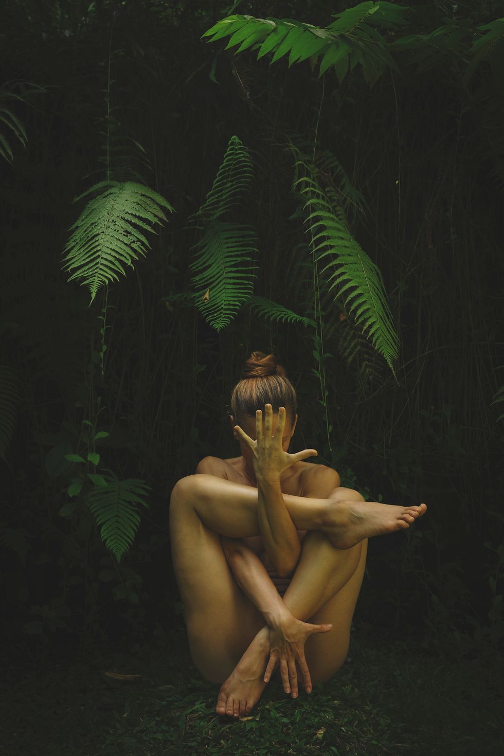 naked mid adult woman exercising against plants at park