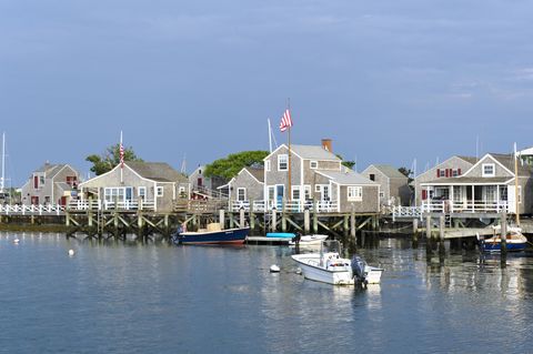 a harbor with buildings in the background, one with an american flag, and several boats in the water