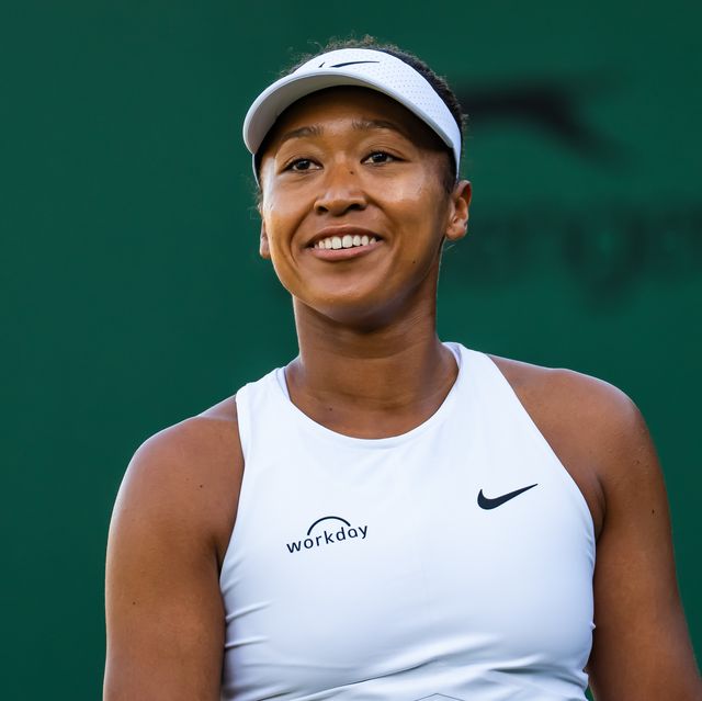 woman in white tank top and visor looking up and smiling