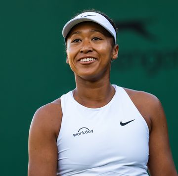 a woman wears a white tank top and visor as she looks up and smiles