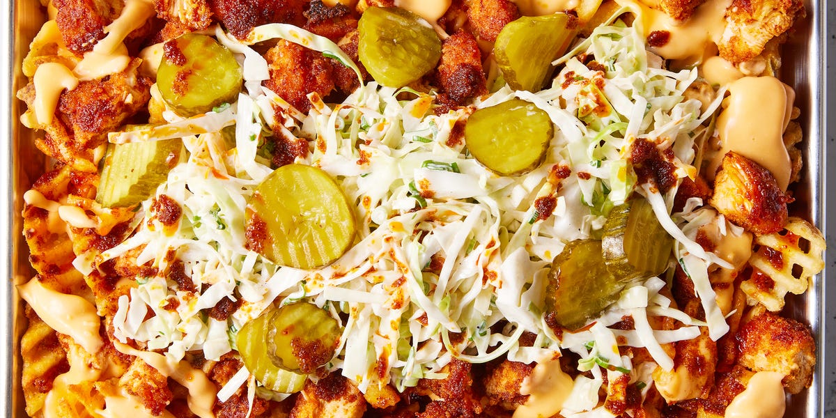 waffle fries layered on a sheet pan topped with nashville hot chicken, cheese, pickles, and slaw
