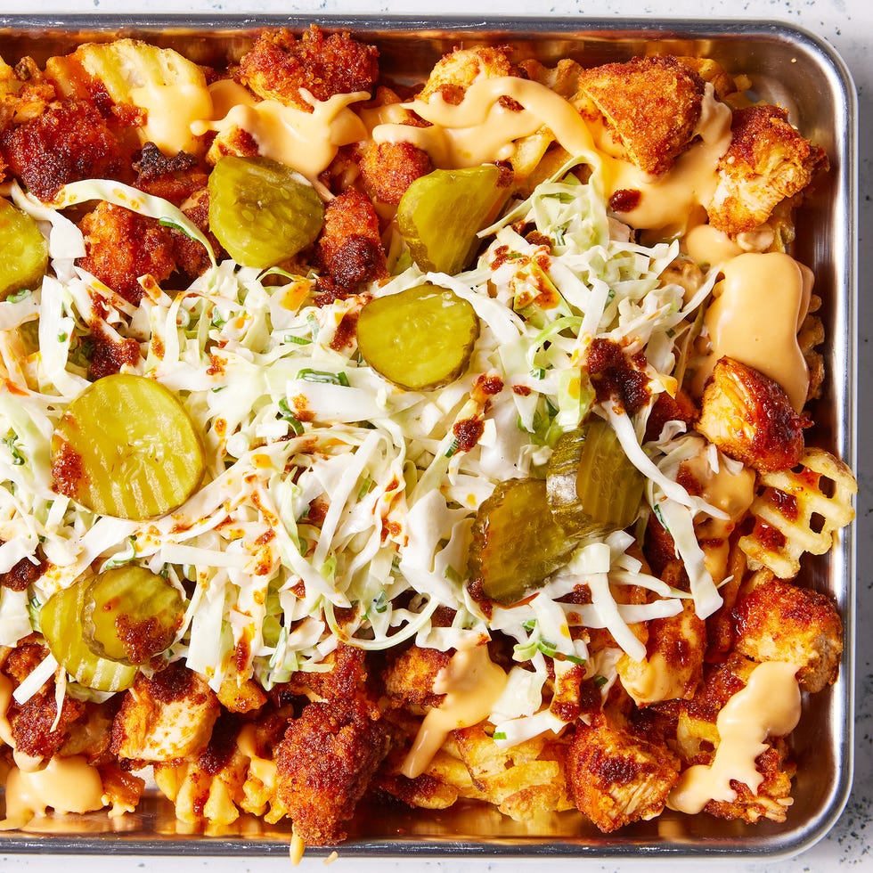 waffle fries layered on a sheet pan topped with nashville hot chicken, cheese, pickles, and slaw