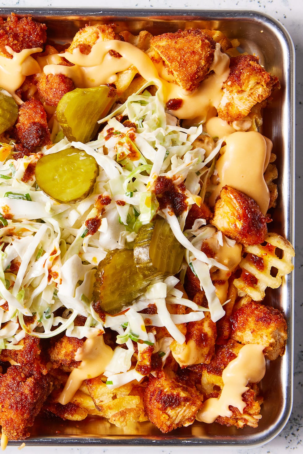 waffle fries layered on a sheet pan topped with nashville hot chicken, cheese, pickles, and slaw