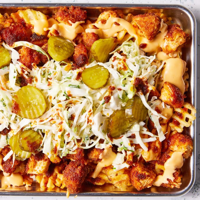 waffle fries layered on a sheet pan topped with nashville hot chicken, cheese, pickles, and slaw