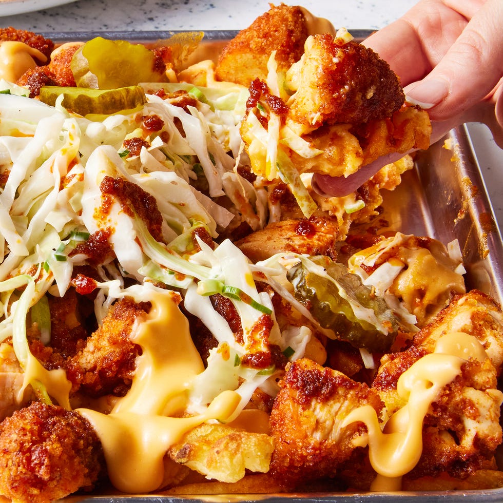 waffle fries layered on a sheet pan topped with nashville hot chicken, cheese, pickles, and slaw