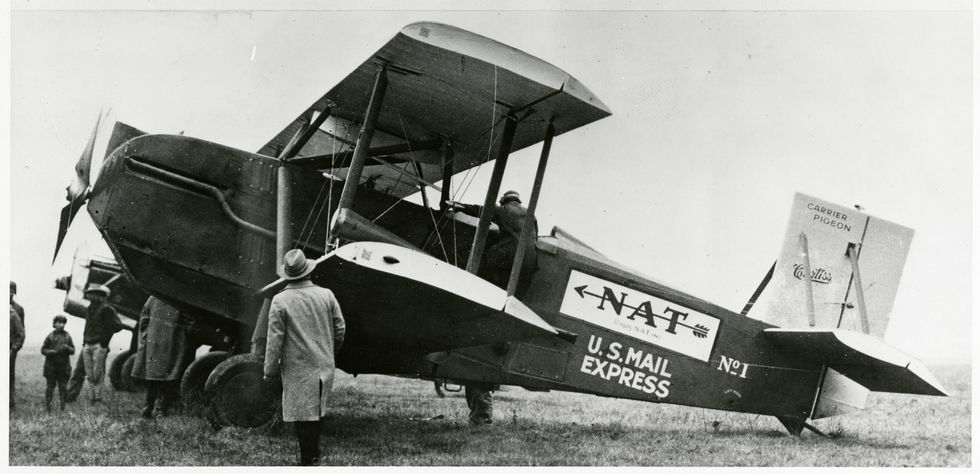 left side view of a curtiss carrier pigeon model 40 aircraft on the ground the aircraft bears the national air transport nat insignia, "us mail express", and "no1" a pilot is climbing into the cockpit