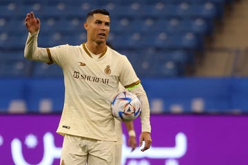 cristiano ronaldo gesturing with his right arm as he holds a soccer ball against his body
