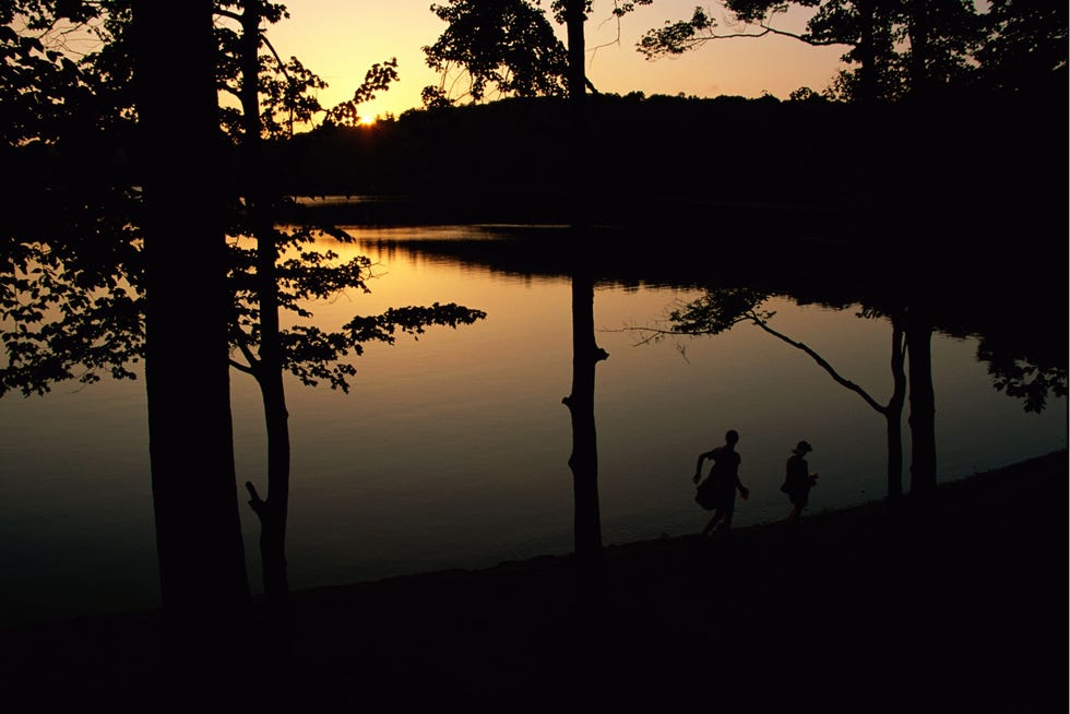 twee mensen lopen in de schemer langs de oever van Walden Pond in de staat Massachusetts