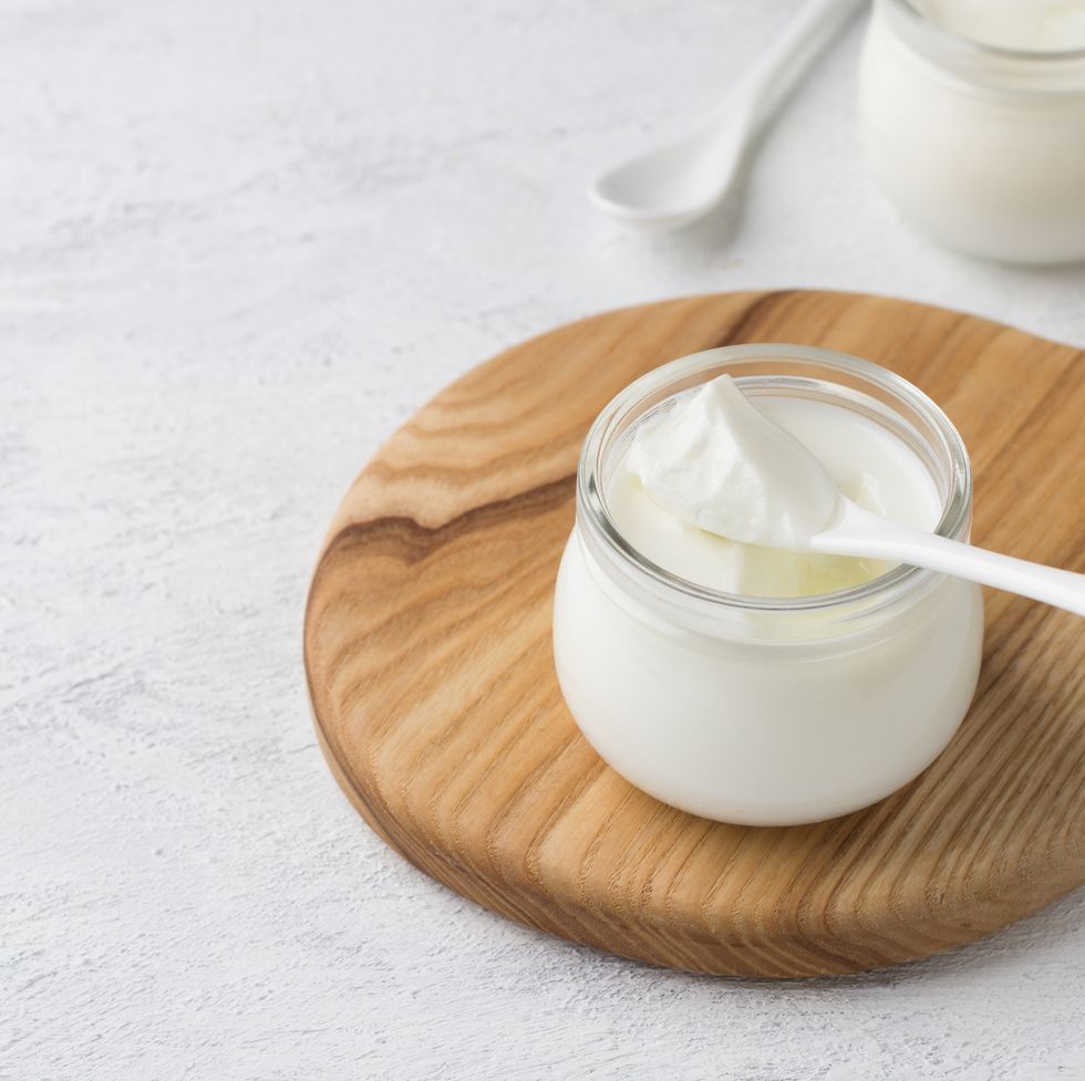 natural homemade yogurt in a glass jar on a wooden board on a light gray background