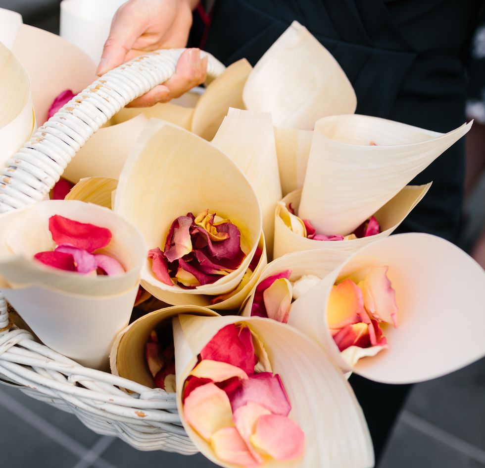 up close image of rose petals in white cones sitting in a basket to be used as confetti at a wedding ceremony