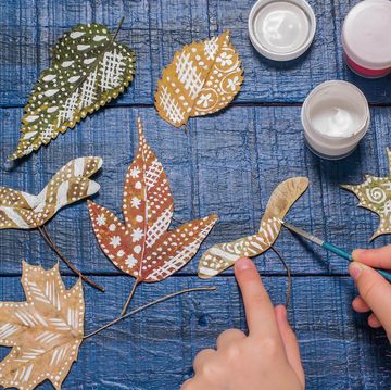 girl paints patterns on autumn leaves on blue background