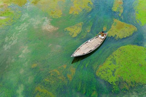 Een man vaart s winters in een bootje op de rivier de Baral In de wintermaanden zijn de rivieralgen zichtbaarder dan in de andere seizoenen