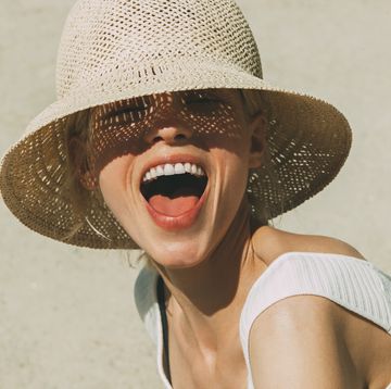 vrouw met mooi gebit en hemd lacht in de camera met zonnehoed op het strand