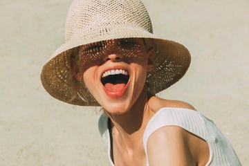 vrouw met mooi gebit en hemd lacht in de camera met zonnehoed op het strand