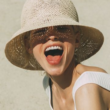 vrouw met mooi gebit en hemd lacht in de camera met zonnehoed op het strand