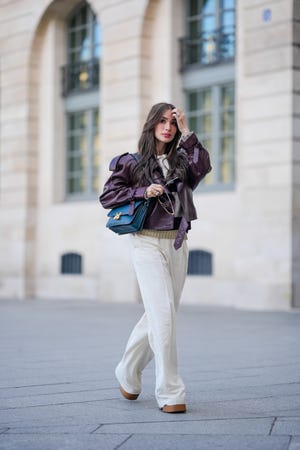 paris, france april 23 heart evangelista wears sunglasses, a purple leather oversized gathered jacket from ysl saint laurent, a blue leather bag, a gray and black striped sweater, white pants from massimo dutti, brown shoes, during a street style fashion photo session, on april 23, 2024 in paris, france photo by edward berthelotgetty images