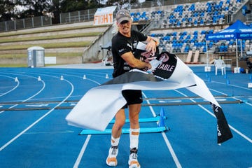 an athlete stands on a blue athletic track, holding a large banner that appears to be in motion