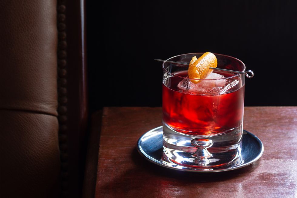negroni cocktail, with gin, red vermouth, and campari, over ice with orange twist in dark luxurious bar