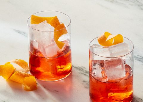 two glasses of negroni cocktails garnished with orange peels on a white marble background